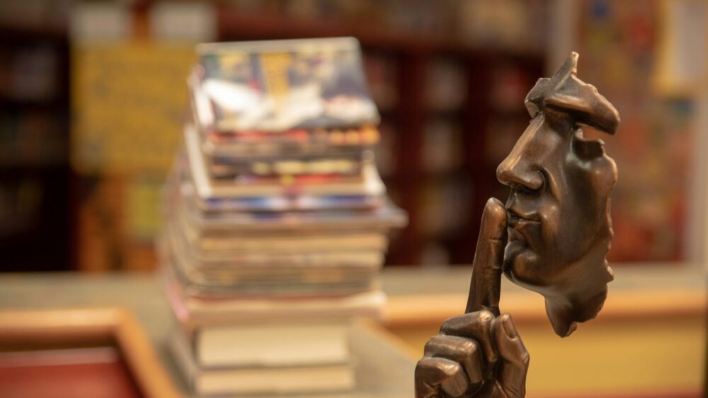 Abstract person with finger over mouth and books in background